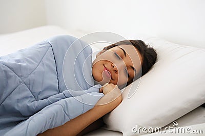 Portrait pretty young woman under the blanket in modern apartment in the morning. She keeps eyes closed and looks satisfied. Stock Photo