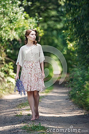 Portrait of pretty young woman walking in a fairy forest with bouquet of flowers. Stock Photo