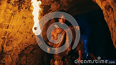 Portrait of Primeval Caveman Wearing Animal Skin Exploring Cave At Night, Holding Torch with Fire Stock Photo