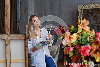 Portrait of a professional artist painting on canvas in the studio. A female artist draws in the workplace. A blonde girl in a Stock Photo