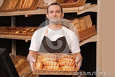 Portrait of professional baker holding tray with fresh buns near showcase Stock Photo