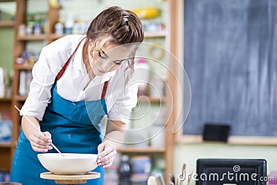 Portrait of Professional Female Ceramist in Apron Glazing Ceramic Bowl on Turntable in Workshop. Stock Photo