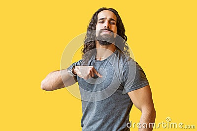 Portrait of proud bearded young man with long curly hair in grey tshirt standing, pointing himself and looking at camera with Stock Photo