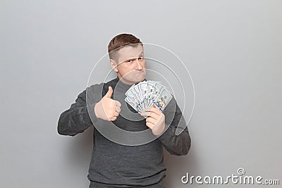 Portrait of proud serious man holding dollars and raising thumb up Stock Photo