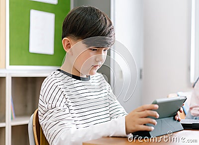 Portrait of pupil little boy concentrating with digital tablet while sitting at desk with classmates in classroom at elementary Stock Photo