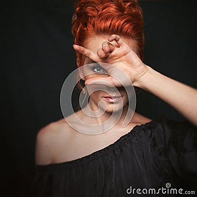 Portrait of redhead woman with blue eyes. Girl looks directly into the camera through her fingers. Stock Photo