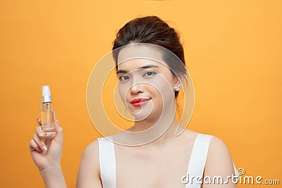Portrait of relaxed pretty female holding a bottle of drops of cosmetic oil isolated on vivid yellow background Stock Photo