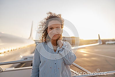 Portrait of relaxed woman smiling at camera while standing outdoors ready for boarding the plane at sunset Stock Photo