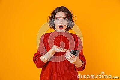 Portrait of resentful woman holding and using cell phone while standing isolated over yellow background Stock Photo