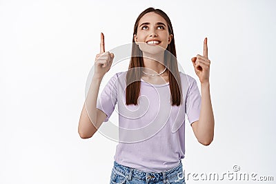 Portrait of 25s woman pointing and looking up with satisfied white smile, showing advertisement, making her choice Stock Photo