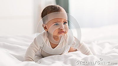 Portrait of sad black baby crying and crawling on bed Stock Photo