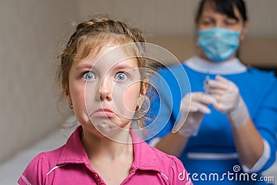 Portrait of a sad child on the background of a nurse in a medical mask. Little girl is afraid of vaccination. Kid does not want to Stock Photo