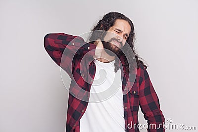 Portrait of sad handsome man with beard and black long curly hair in casual style, checkered red shirt standing and holding his p Stock Photo