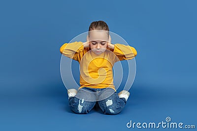 Portrait of sad little girl sitting on blue studio background, autism concept Stock Photo