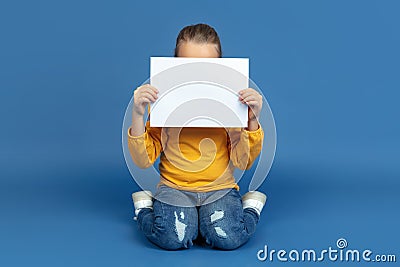 Portrait of sad little girl sitting on blue studio background, autism concept Stock Photo
