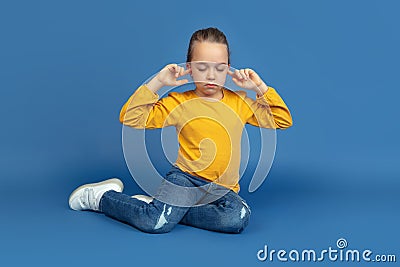 Portrait of sad little girl sitting on blue studio background, autism concept Stock Photo