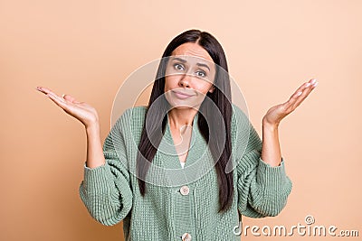 Portrait of sad unsure girl hands up shrug shoulders wear green sweater isolated on peach color background Stock Photo