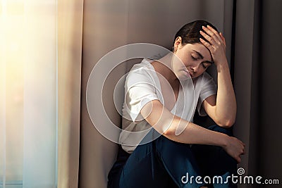 Portrait of a sad woman, clutching her head, sitting in the corner of the apartment. Copy space. The concept of domestic violence Stock Photo