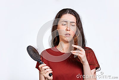 Portrait of a saddened brunette woman holds a comb with hair falling out and looks at the tips of her hair.White background Stock Photo