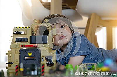 Portrait of School boy lying down on the carpet floor playing with soldiers, military car and figurine toys, Happy Kid playing Stock Photo