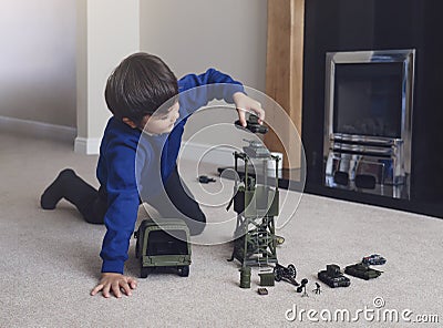 Portrait of School boy sitting on carpet floor playing with soldiers, military car and figurine toys, Happy Kid playing wars and Stock Photo