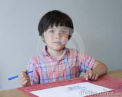 Portrait of school kid boy siting on table doing homework, Happy Child holding blue colour paint,A boy drawing blue colour on whit Stock Photo