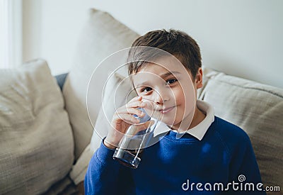 Portrait schoolboy drinking soda or soft drink with glass,Child enjoying cold fizzy dink while watching TV after back from school, Stock Photo
