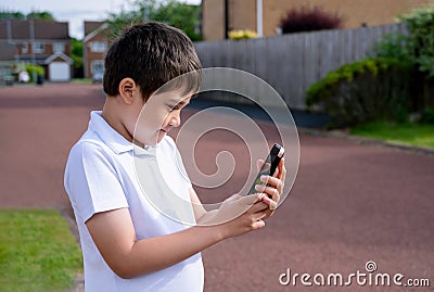 Portrait schoolboy using smartphone typing text messages, Happy kid standing outdoor using cellphone chatting with friends,Child Stock Photo