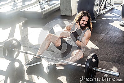Portrait of screaming young adult man athlete with long curly hair working out in gym, sitting on floor and have strong hurt Stock Photo