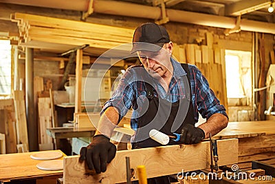 Portrait of a senior carpenter in uniform gluing wooden bars with hand pressures at the carpentry manufacturing Stock Photo