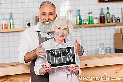 portrait of senior coffee shop owners in aprons holding open chalkboard together Stock Photo