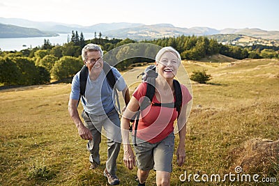 Portrait Of Senior Couple Climbing Hill On Hike Through Countryside In Lake District UK Together Stock Photo