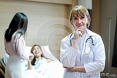 Portrait of senior female doctor in workwear with stethoscope standing and thinking and taking decisions with hand on chin in Stock Photo