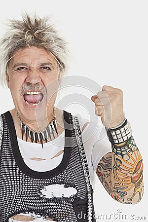 Portrait of senior male punk screaming with clenched fist over gray background Stock Photo