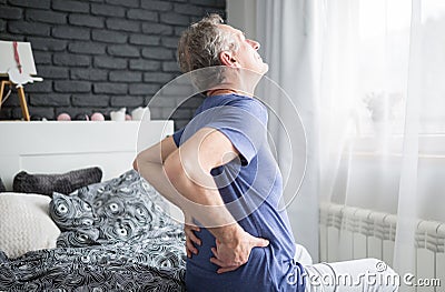 Senior man with lower back pain siting on bed Stock Photo