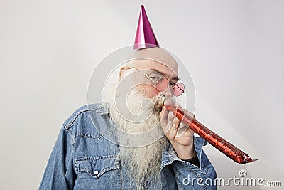 Portrait of senior man wearing party hat while blowing horn against gray background Stock Photo