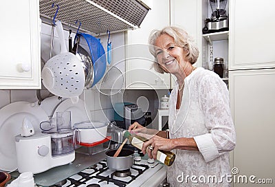 Portrait of senior woman adding olive oil to saucepan at kitchen counter Stock Photo