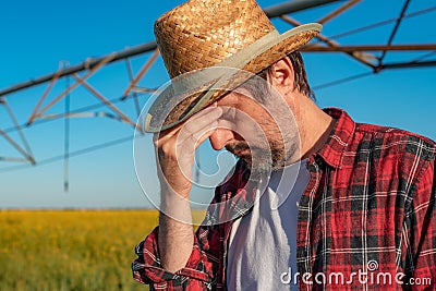 Portrait of serious farmer standing in front of center-pivot irrigation equipment in rapeseed field Stock Photo