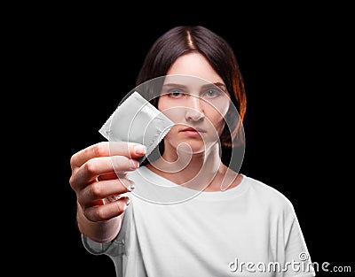 A close-up of a serious young woman showing a packed condom on a black background. Healthy lifestyle concept. Copy space Stock Photo