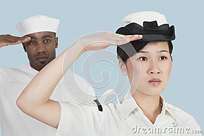 Portrait of serious female US Navy officer and male sailor saluting over light blue background Stock Photo