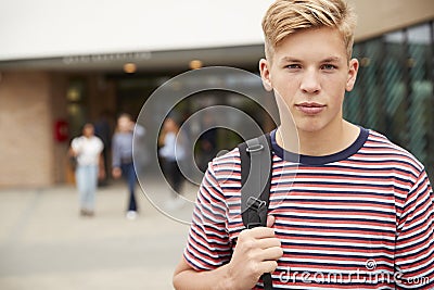 Portrait Of Serious Male High School Student Outside College Building With Other Teenage Students In Background Stock Photo