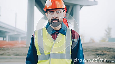 portrait of serious surveyor standing in building area with theodolite in background Stock Photo