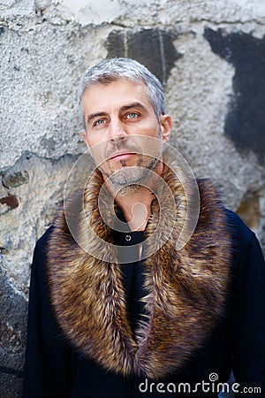 Portrait of a man in wolf fur and thoughtful expression on his face, a structure wall on background Stock Photo