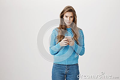 Portrait of and stylish european adult woman with broad smile and sensual look holding smartphone while standing Stock Photo