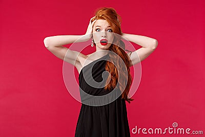 Portrait of shocked and ambushed young redhead female in elegant black dress, gasping nervously, look alarmed camera Stock Photo