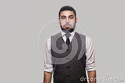 Portrait of shocked handsome bearded brunette man in white shirt and waistcoat standing and looking at camera with big eyes and Stock Photo