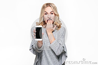 Portrait of shocked pretty blond woman with hand on her mouth showing mobile phone blank screen isolated over white background. Stock Photo