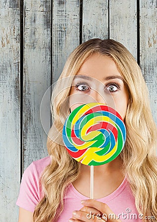 Portrait of shocked woman covering mouth with candy against wooden wall Stock Photo