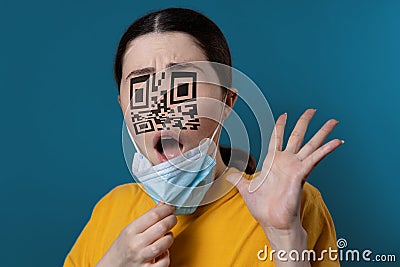 Portrait of a shocked woman with a QR code instead of eyes and nose, removing protective mask from her face. Blue Stock Photo