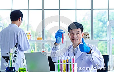 Portrait shot of Asian professional mature male scientist in white lab coat and rubber gloves sitting look at camera smiling Stock Photo